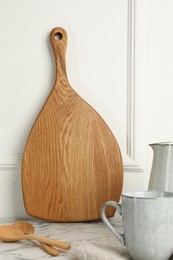 Photo of Wooden cutting board, spoons and dishware on white marble table