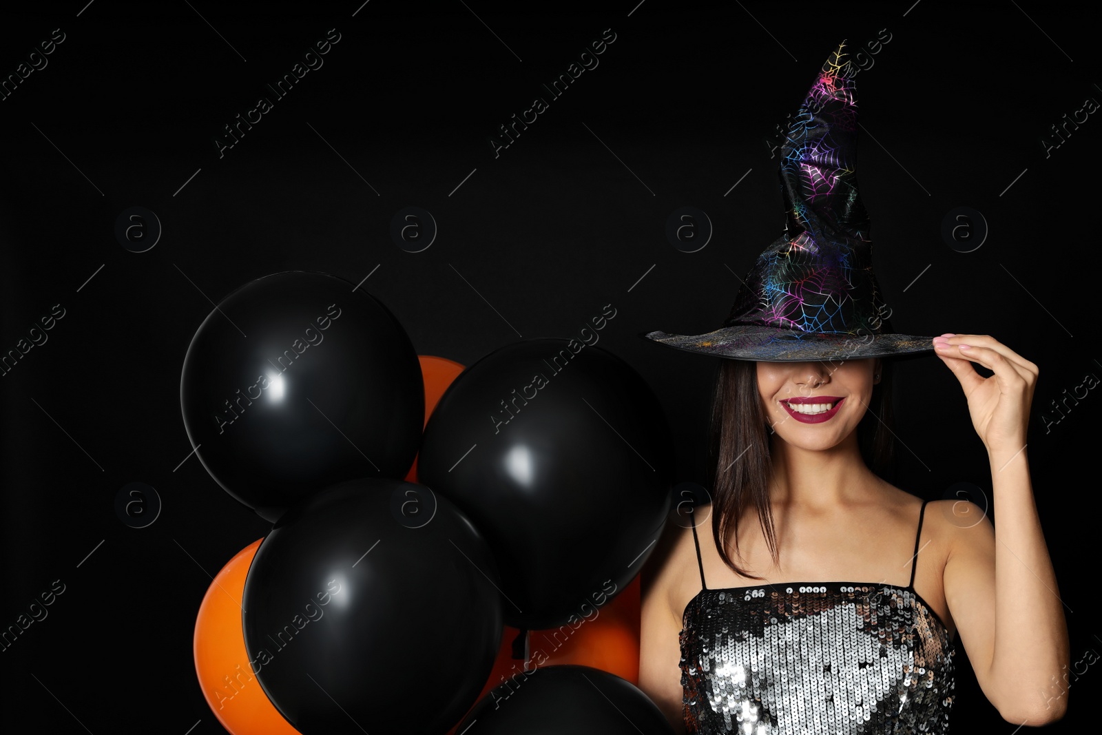 Photo of Beautiful woman wearing witch costume with balloons for Halloween party on black background