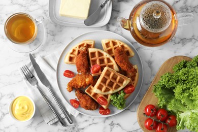 Photo of Tasty Belgian waffles served with fried chicken, tomatoes, lettuce and tea on white marble table, flat lay