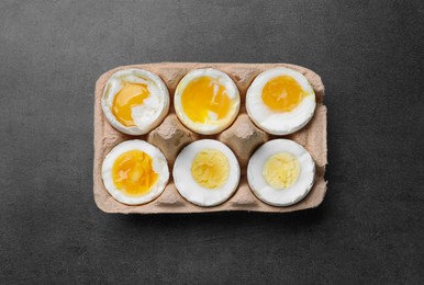 Photo of Boiled chicken eggs of different readiness stages in carton on dark grey table, top view