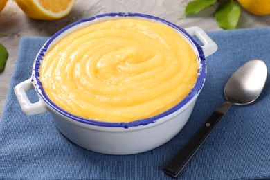 Photo of Delicious lemon curd in bowl and spoon on table, closeup