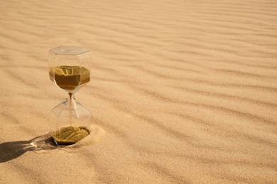 Photo of Hourglass with flowing sand in desert on sunny day. Space for text