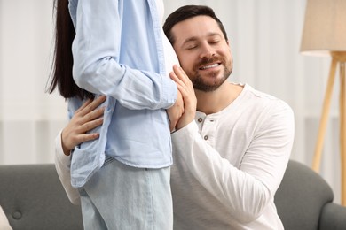 Photo of Happy husband listening pregnant wife's belly at home