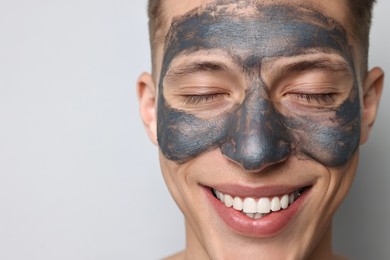 Photo of Handsome man with clay mask on his face against light grey background, closeup. Space for text