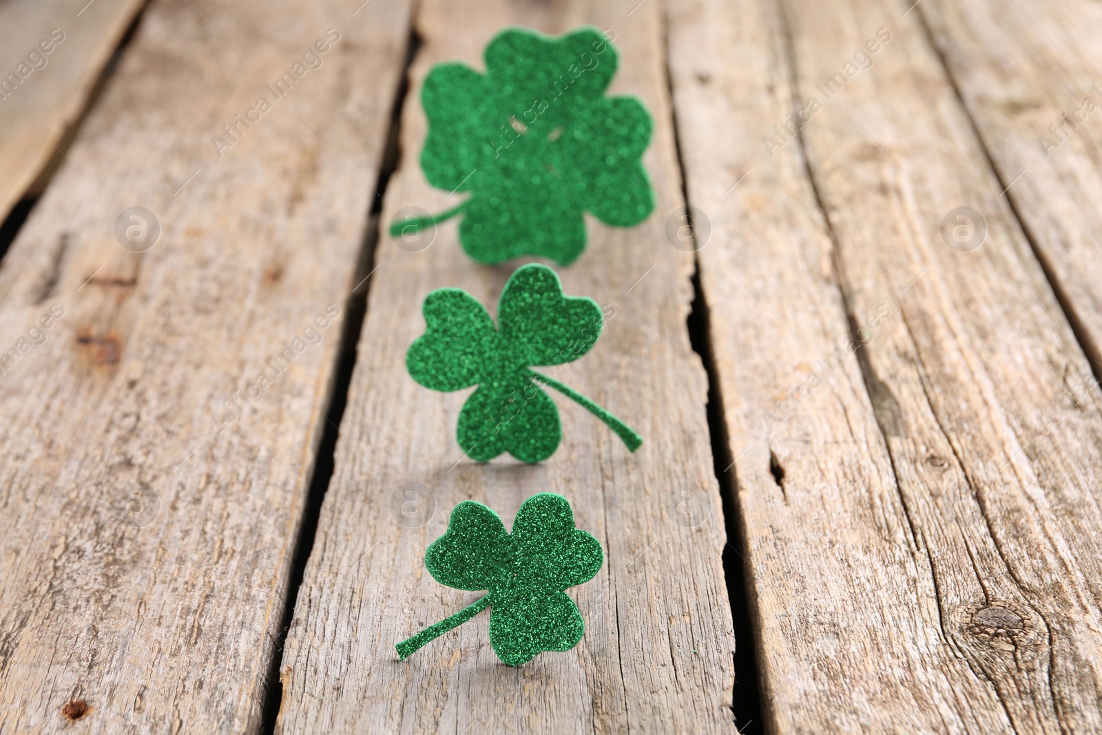 Photo of St. Patrick's day. Shiny decorative clover leaves on wooden table, selective focus