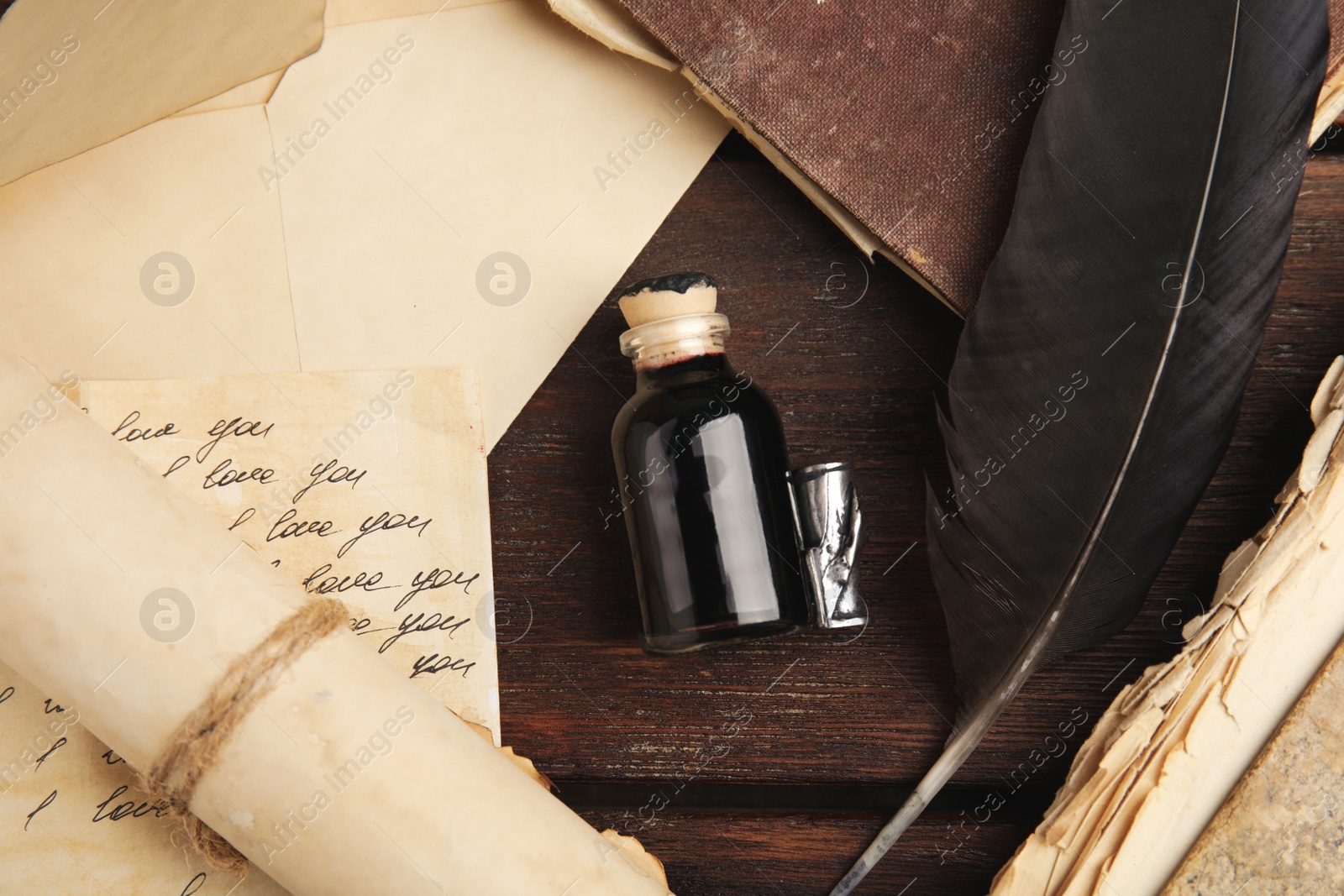 Photo of Feather pen, bottle of ink and paper on wooden table, flat lay