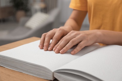 Photo of Blind woman reading book written in Braille at table, closeup