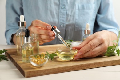 Woman dropping CBD oil or THC tincture into bowl at white wooden table, closeup