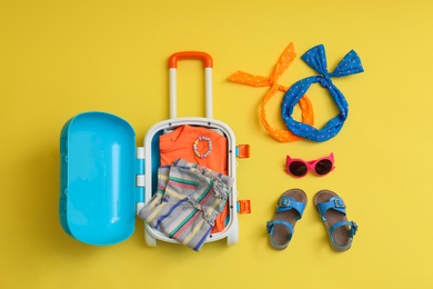 Photo of Flat lay composition with blue suitcase and child accessories on yellow background. Summer vacation