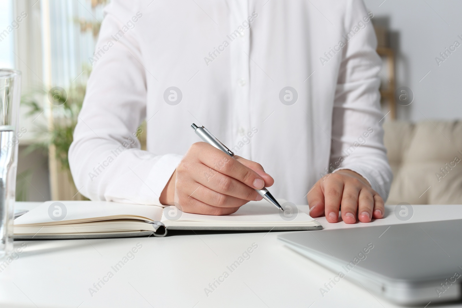 Photo of Woman writing in notebook at white table in office, closeup