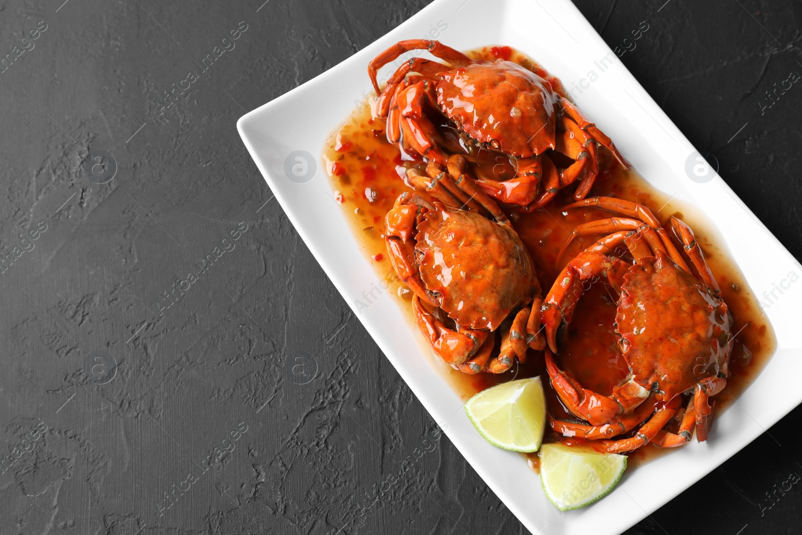 Photo of Delicious boiled crabs with sauce and lime on black textured table, top view. Space for text