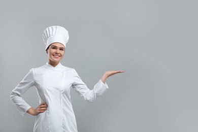 Happy female chef pointing at something on light grey background. Space for text