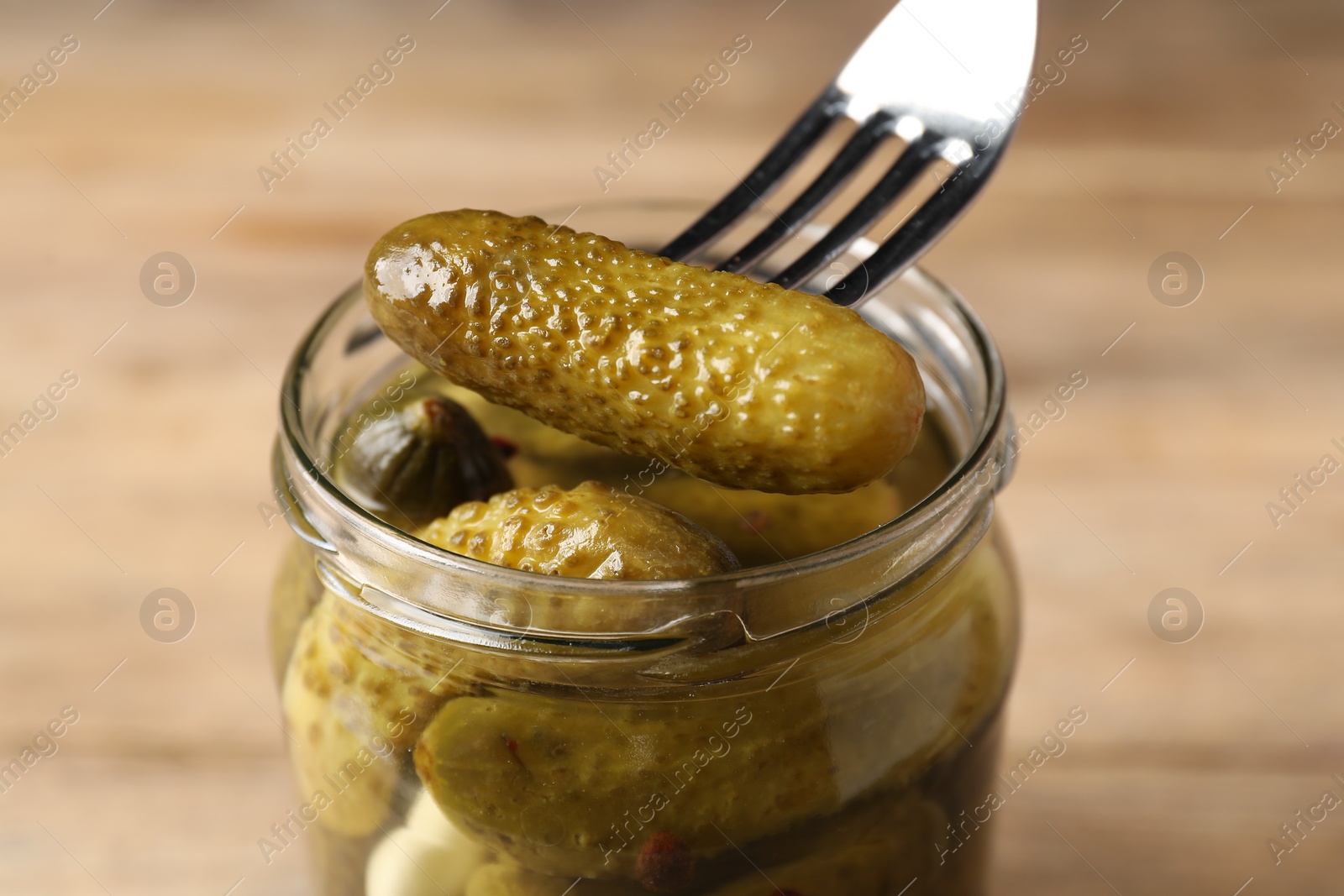 Photo of Eating tasty pickled cucumber from jar at table, closeup