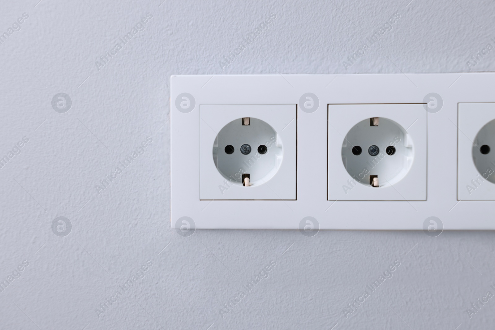 Photo of Electric power sockets on light grey wall indoors, closeup