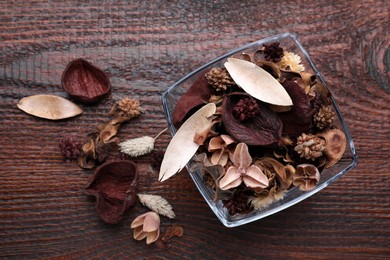 Aromatic potpourri of dried flowers in glass bowl on wooden table, flat lay. Space for text