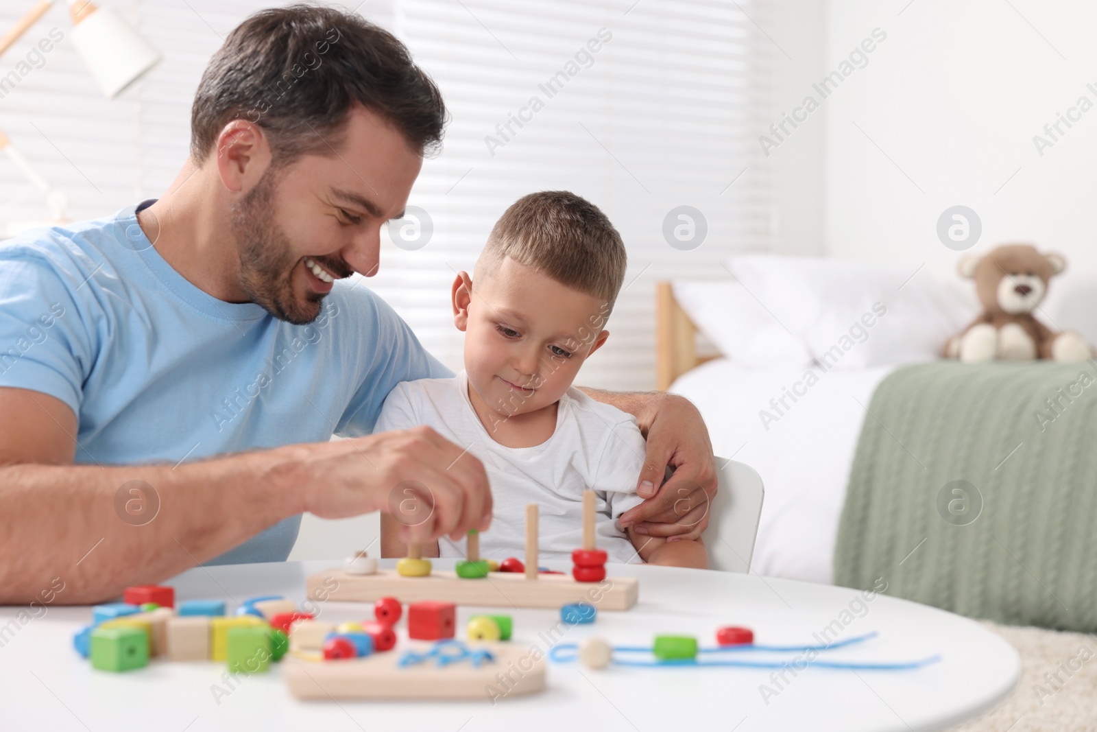 Photo of Motor skills development. Father and his son playing with stacking and counting game at table indoors