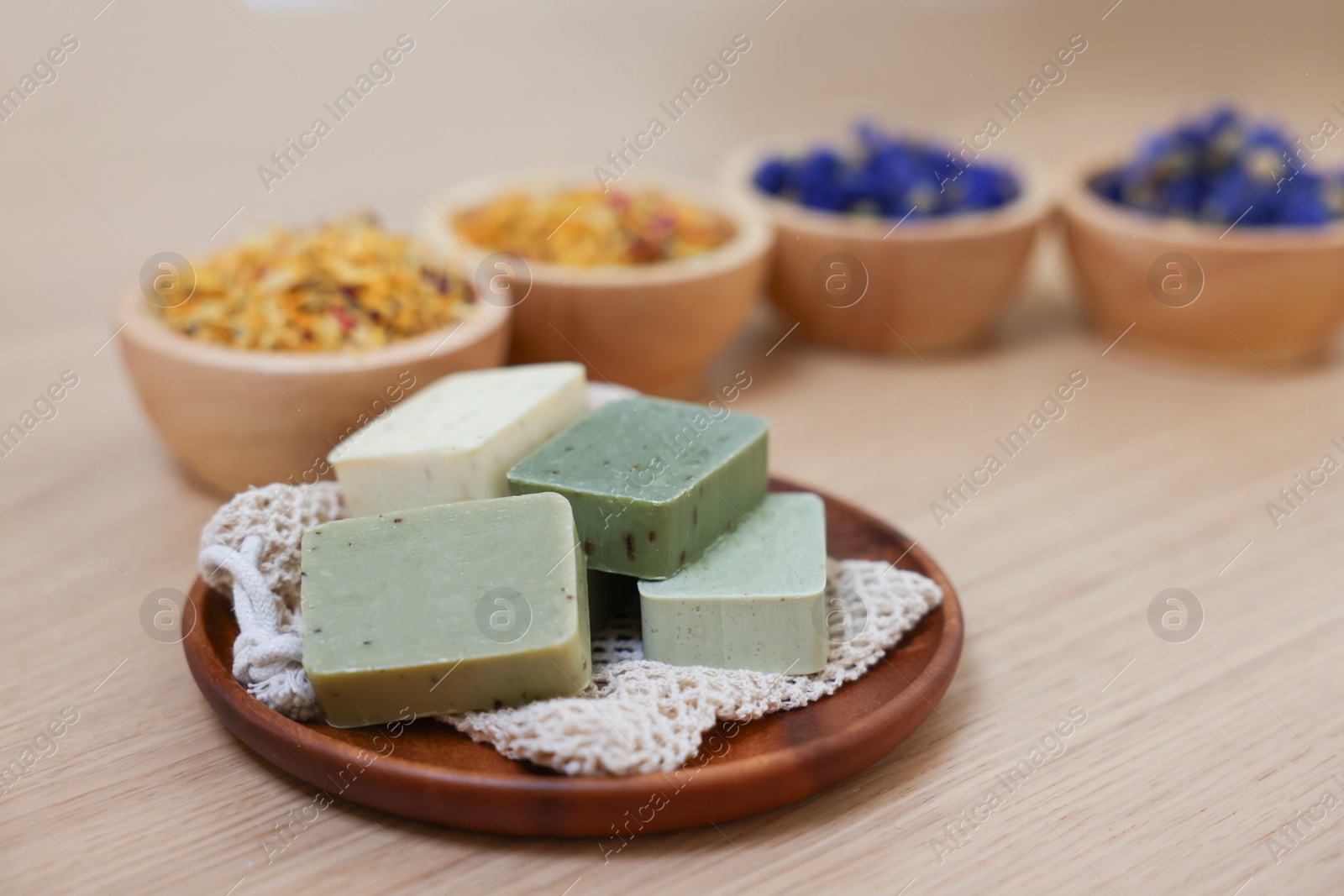Photo of Tray with soap bars and bowls of dry flowers on light wooden table. Spa therapy