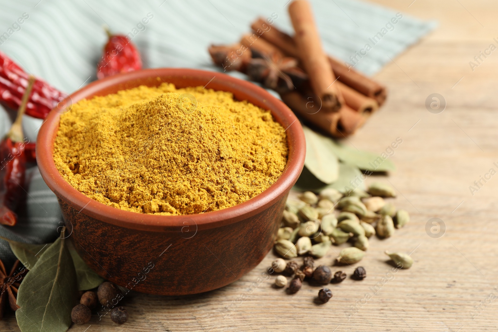 Photo of Curry powder in bowl and other spices on wooden table, closeup. Space for text