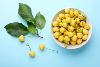 Photo of Bowl and ripe yellow cherries with green leaves on turquoise background, flat lay