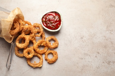 Homemade crunchy fried onion rings and tomato sauce on light background, top view. Space for text