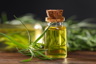 Photo of Bottle of essential oil and fresh tarragon leaves on wooden table, closeup