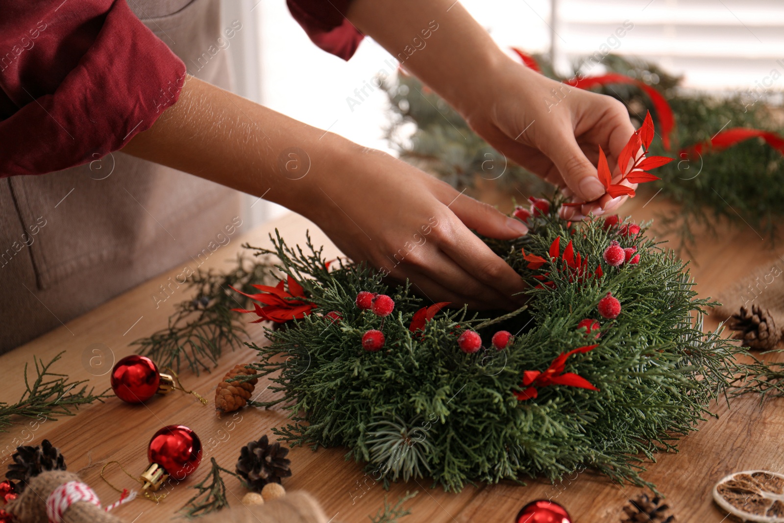 Photo of Florist making beautiful Christmas wreath with berries and red leaves at wooden table indoors, closeup