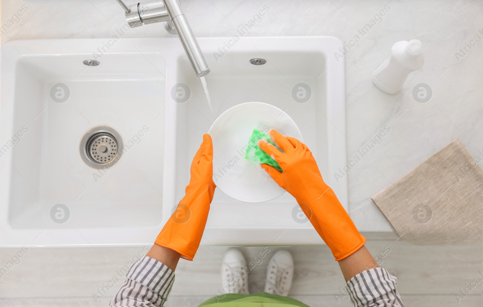 Photo of Woman washing plate above sink in modern kitchen, top view