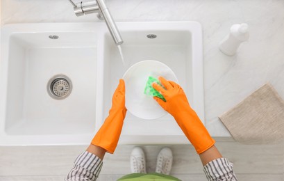 Woman washing plate above sink in modern kitchen, top view