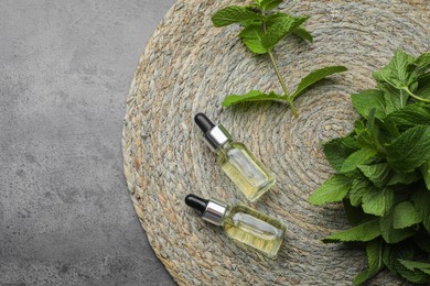 Photo of Bottles of essential oil and mint on grey table, top view. Space for text