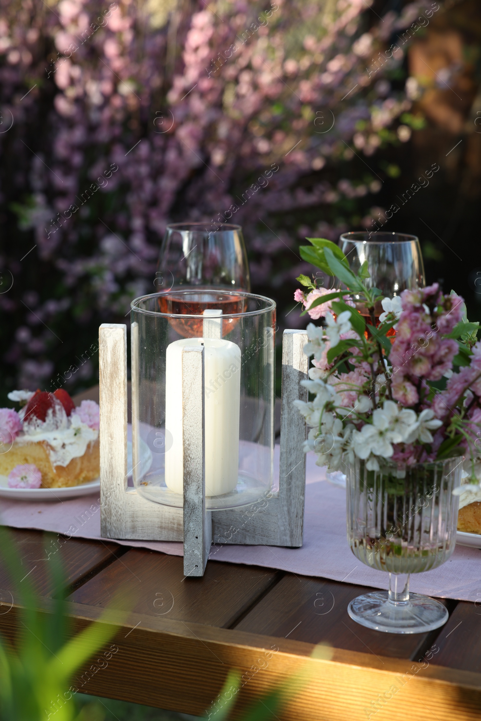 Photo of Vase with spring flowers and candle on table served for romantic date in garden