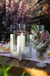 Photo of Vase with spring flowers and candle on table served for romantic date in garden