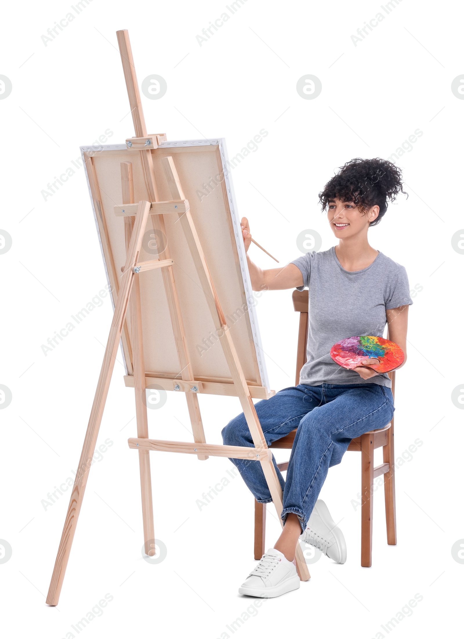 Photo of Young woman painting on easel with canvas against white background