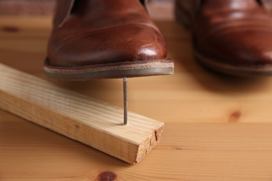 Photo of Metal nail in wooden plank and shoes on table, closeup