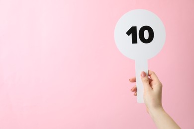 Woman holding auction paddle with number 10 on pink background, closeup. Space for text