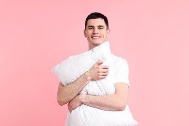 Happy man in pyjama holding pillow on pink background