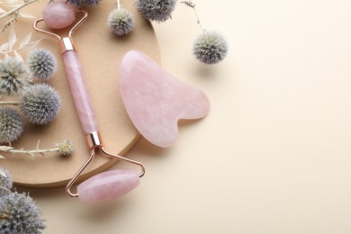 Photo of Flat lay composition with rose quartz gua sha tool and facial roller on beige background. Space for text