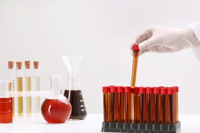 Photo of Scientist putting test tube with brown liquid into stand on white table, closeup