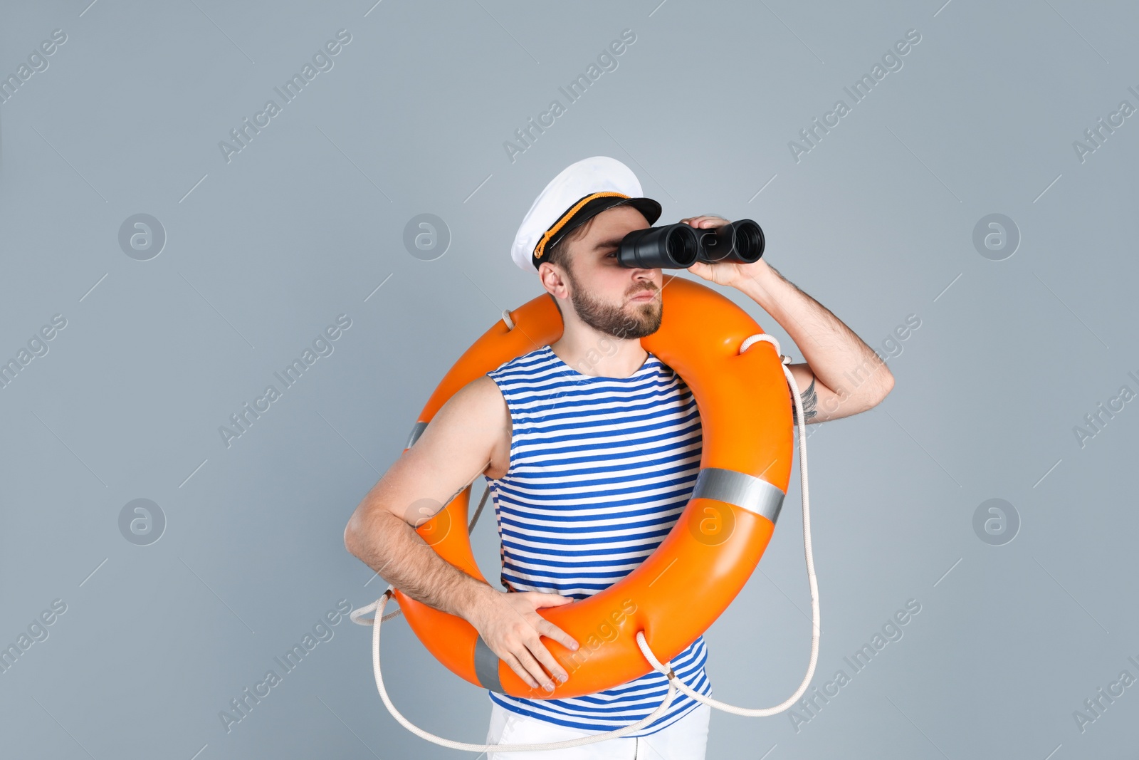 Photo of Sailor with binoculars and ring buoy on light grey background