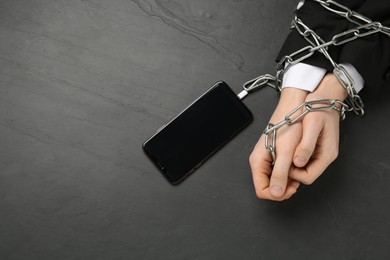 Photo of Man showing chained hands to smartphone at black table, top view. Internet addiction