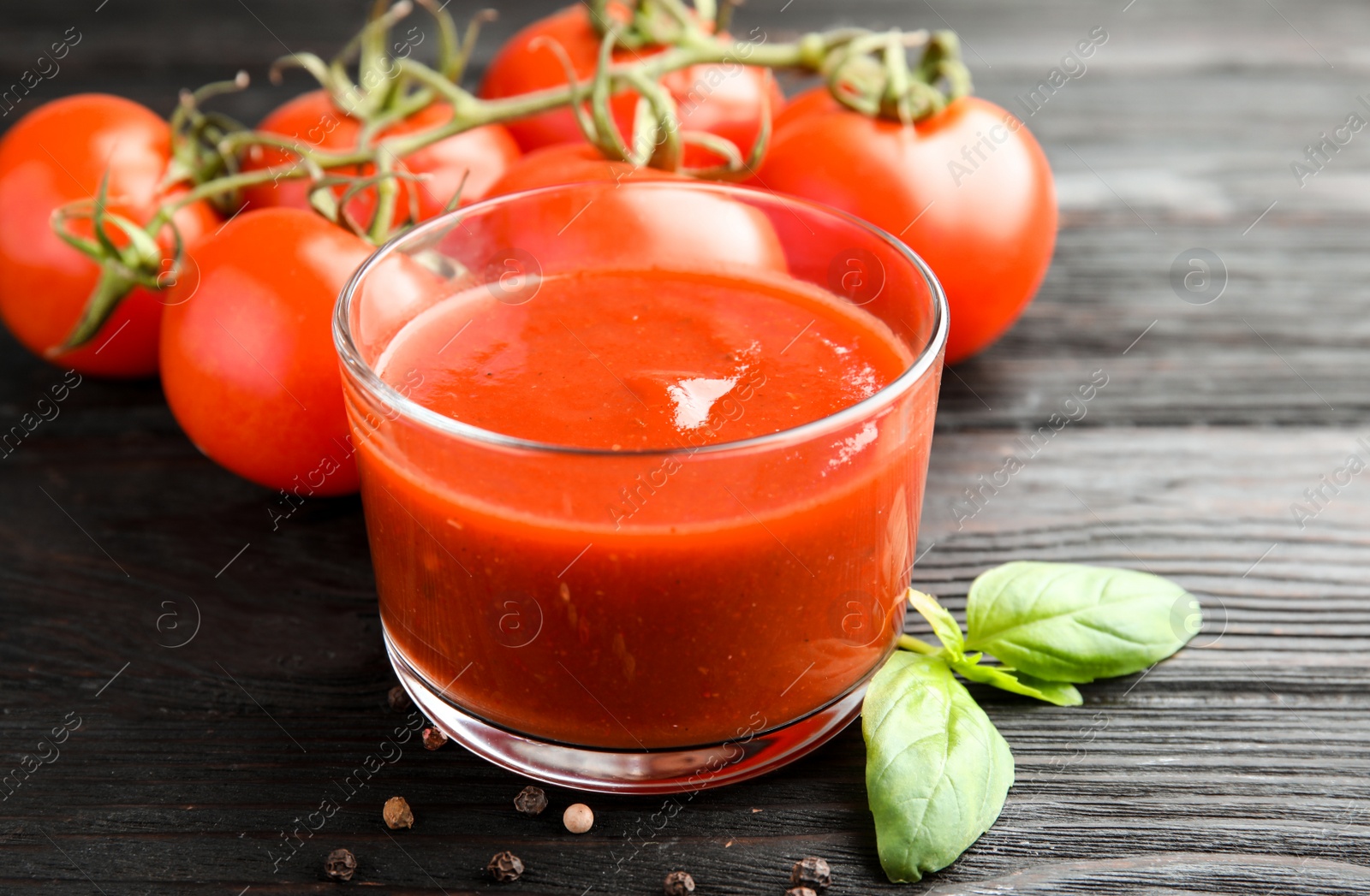 Photo of Glass of tomato sauce with basil on wooden table, closeup