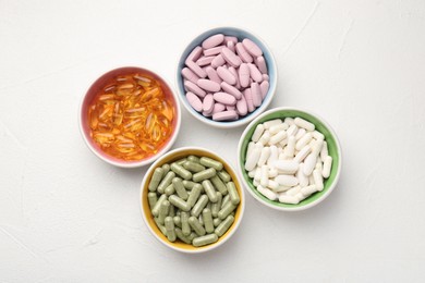 Different vitamin capsules in bowls on white wooden table, flat lay