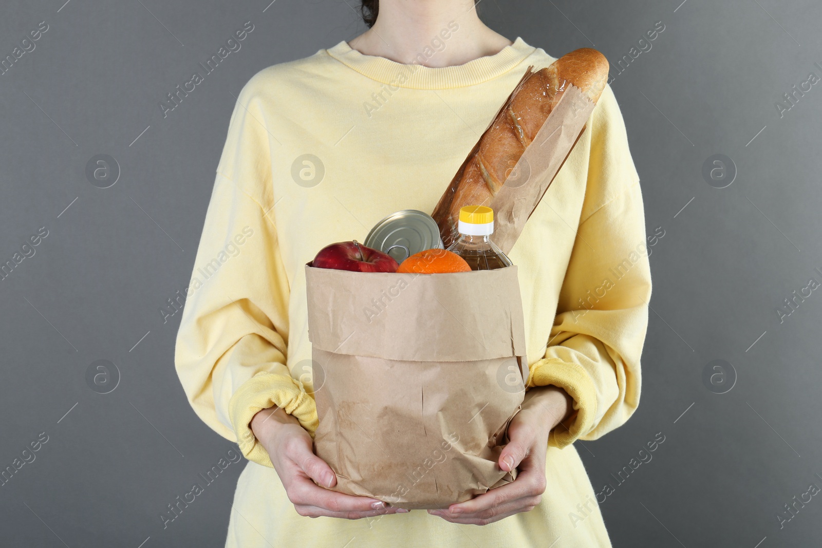 Photo of Humanitarian aid. Woman with food products for donation on grey background, closeup