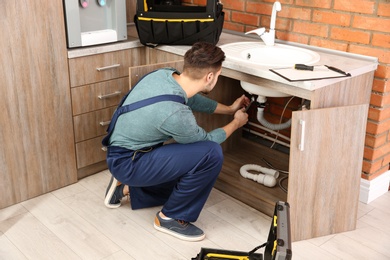 Male plumber in uniform repairing kitchen sink