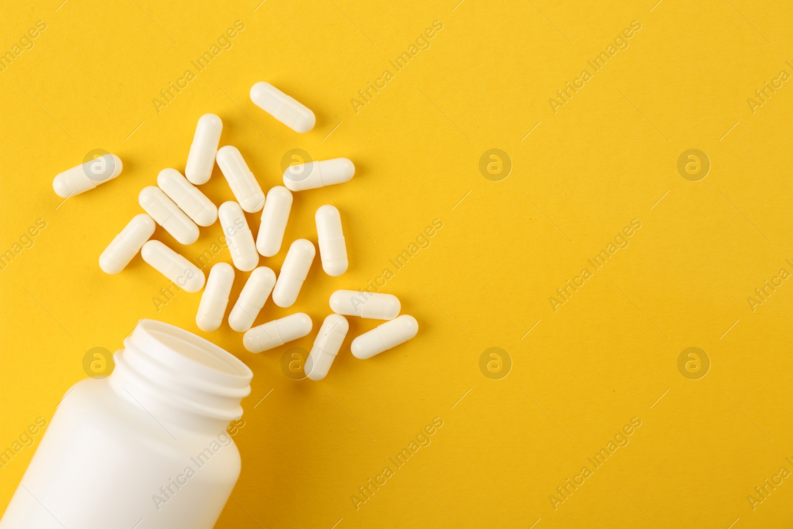 Photo of Bottle and vitamin capsules on yellow background, top view. Space for text