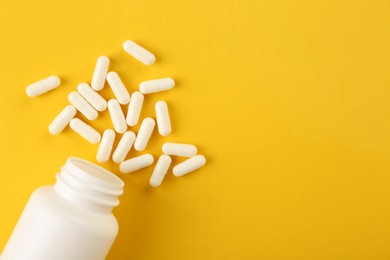 Photo of Bottle and vitamin capsules on yellow background, top view. Space for text