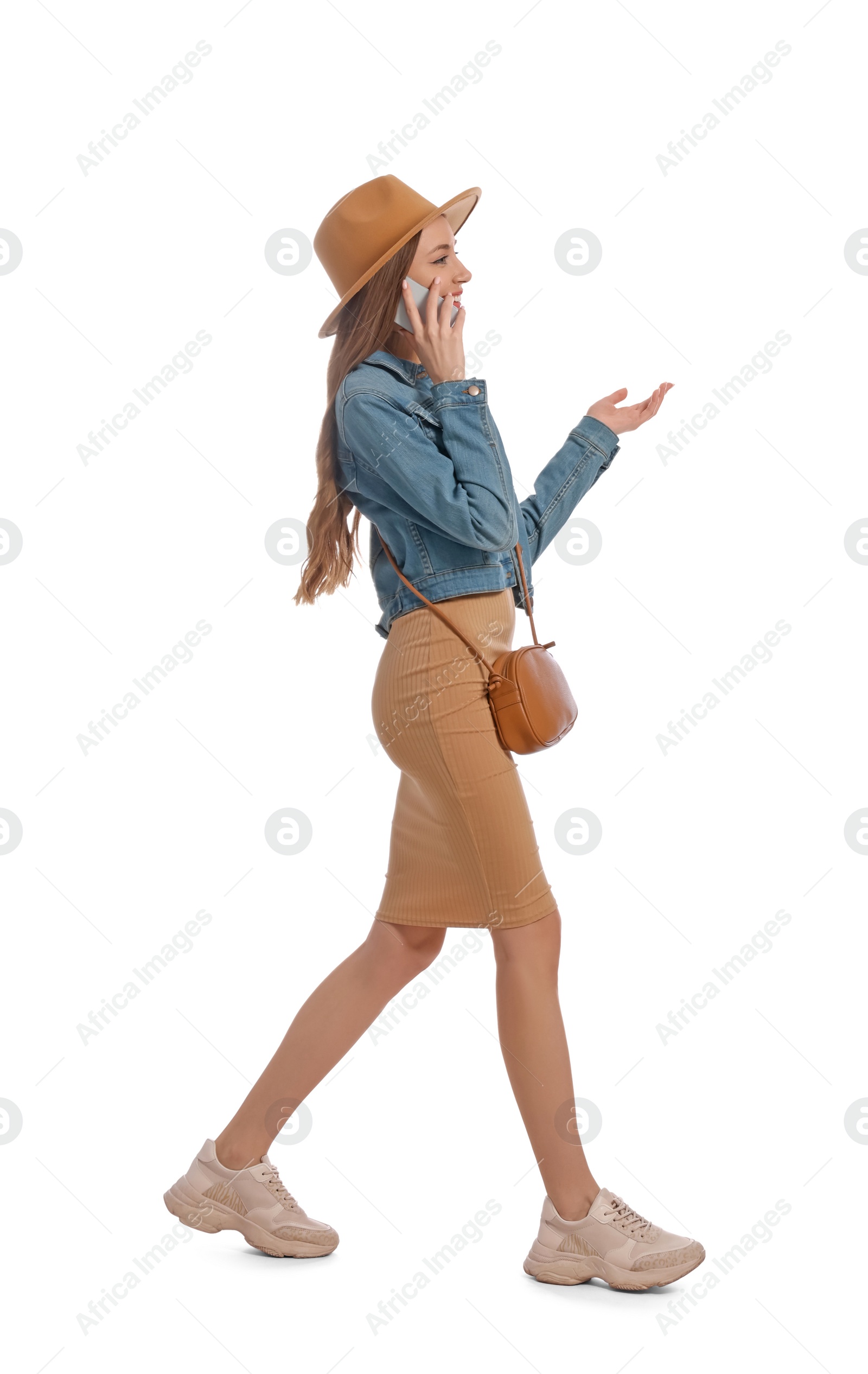 Photo of Young woman in casual outfit talking on smartphone while walking against white background