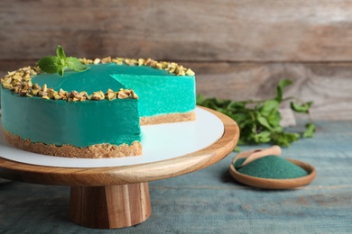 Photo of Dessert stand with tasty spirulina cheesecake on blue wooden table, space for text