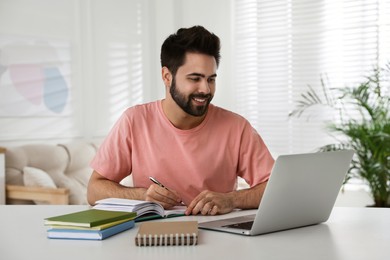 Young man watching webinar at table in room