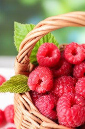 Photo of Tasty ripe raspberries and green leaves in wicker basket, closeup