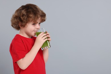 Photo of Cute little boy drinking fresh juice on light gray background, space for text